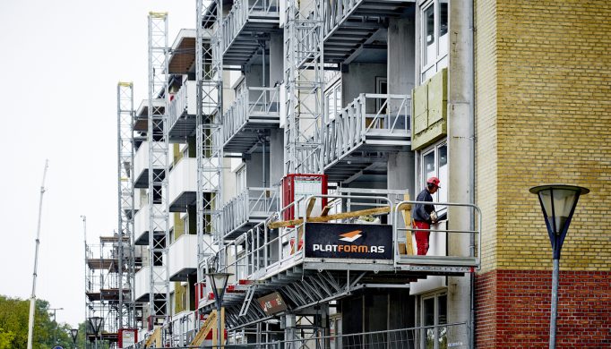 Mand står og arbejder på en arbejdsplatform monteret på siden af et byggeri i Aalborg
